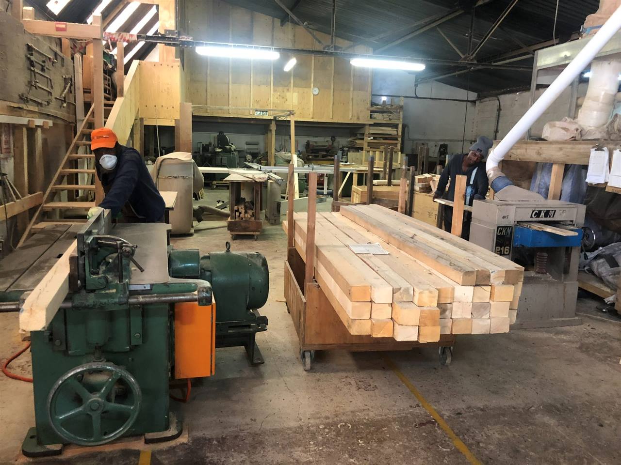 Two operators feeding reclaimed timber through the planers, a trolley of planed beams between them