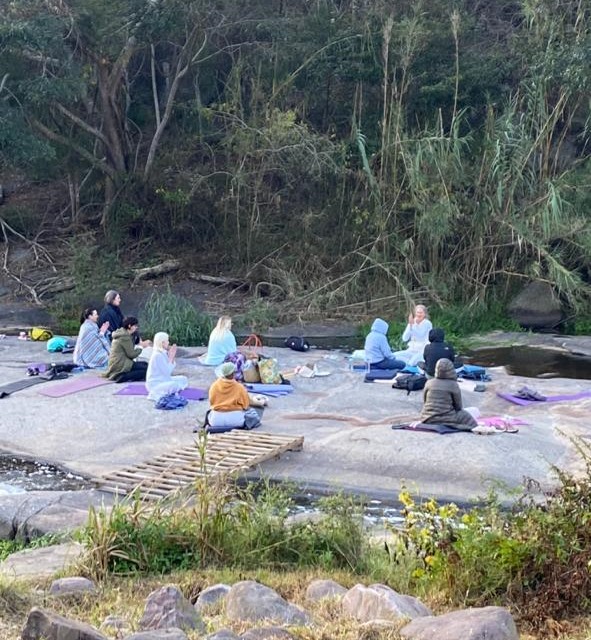 People sitting together on mats on the flat rocks beside the river at Shongweni