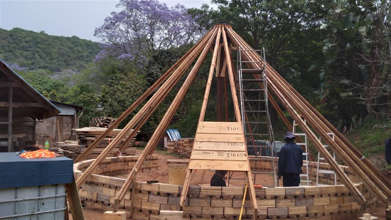 A timber rondavel going up: reclaimed block walls and the roof poles meeting at the top